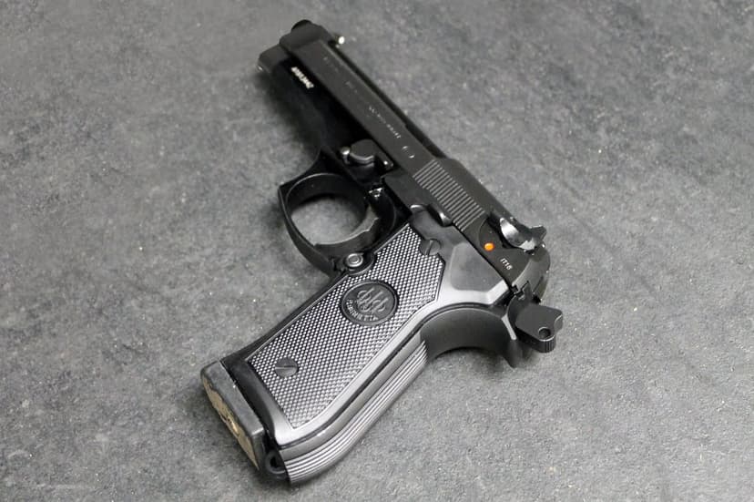 Beretta 92FS semi-automatic pistol with checkered grips on a dark textured surface in a top-down view.