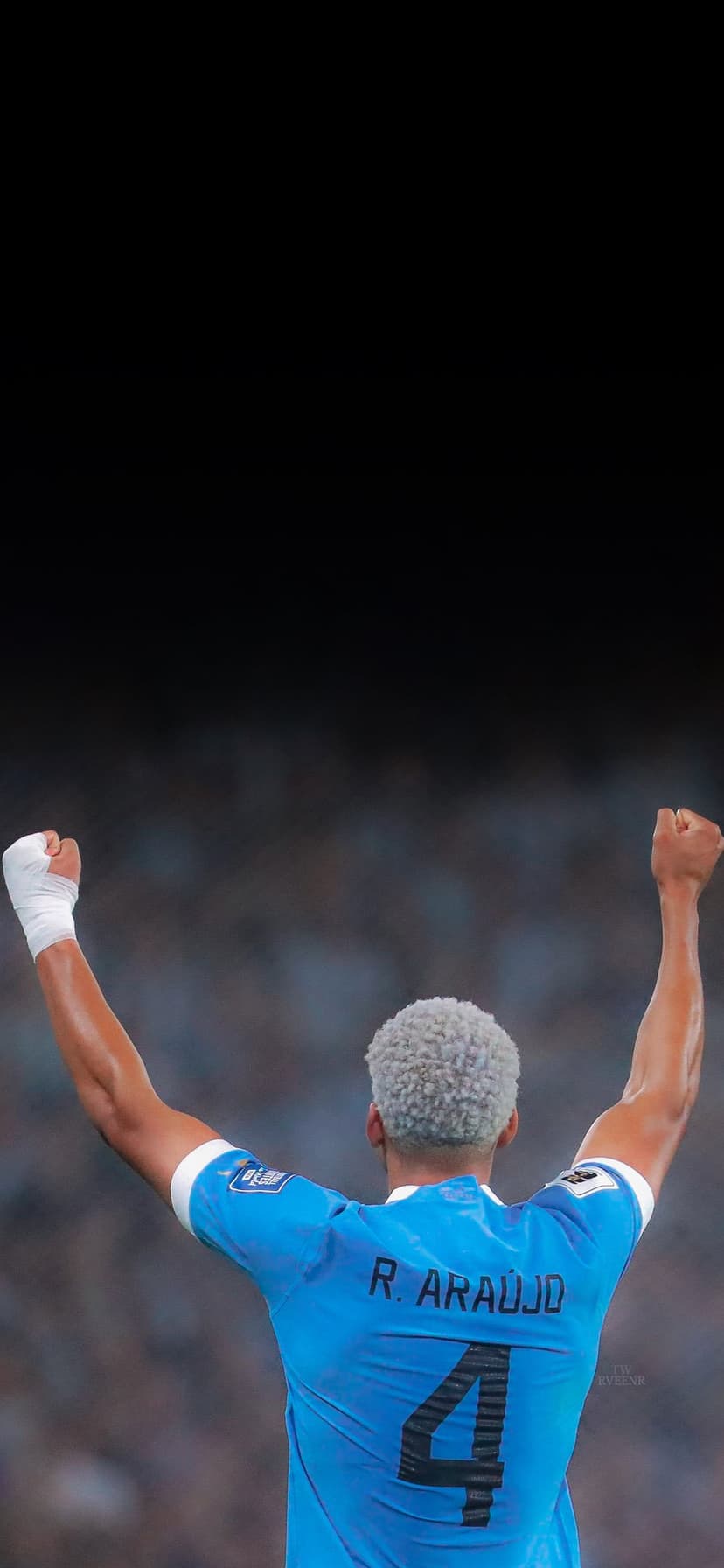 Ronald Araujo raises his arms in celebration wearing a blue number 4 jersey with a blurred stadium background.