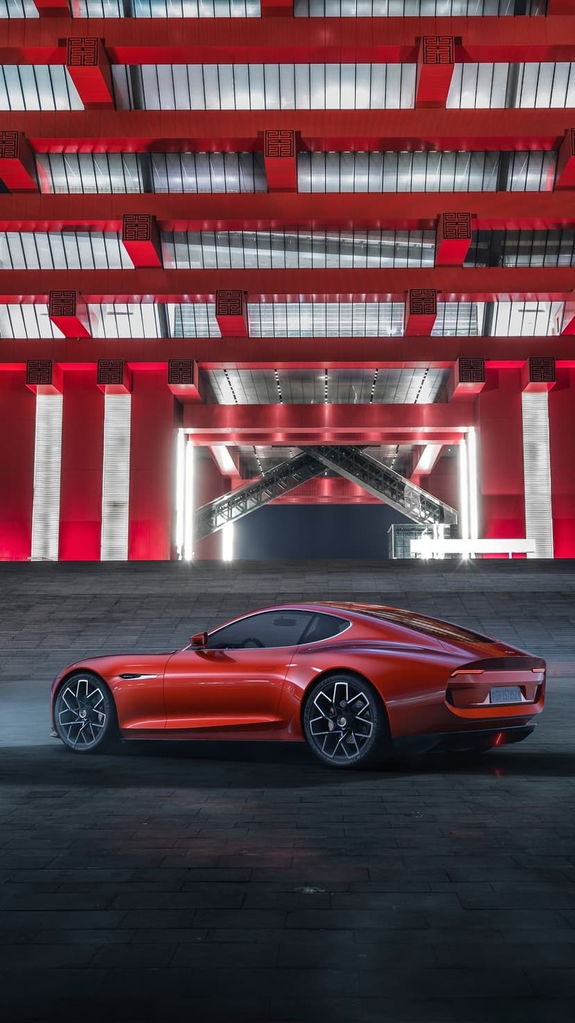 Red concept car parked on asphalt under a modern building with glowing red beams and geometric glass windows.