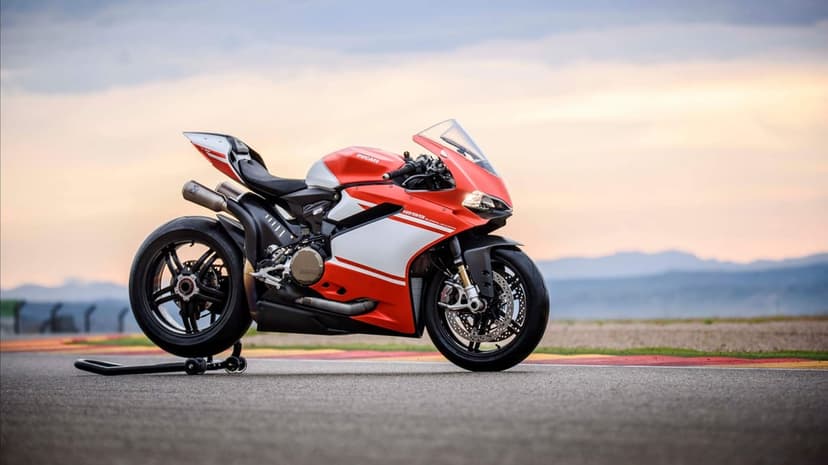 Red and white Ducati 1299 Superleggera motorcycle on a racetrack with a soft sunset sky and mountain backdrop.