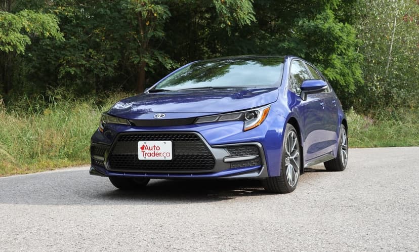 Blue Toyota Corolla hatchback parked on a quiet asphalt road with lush green trees and natural daylight.