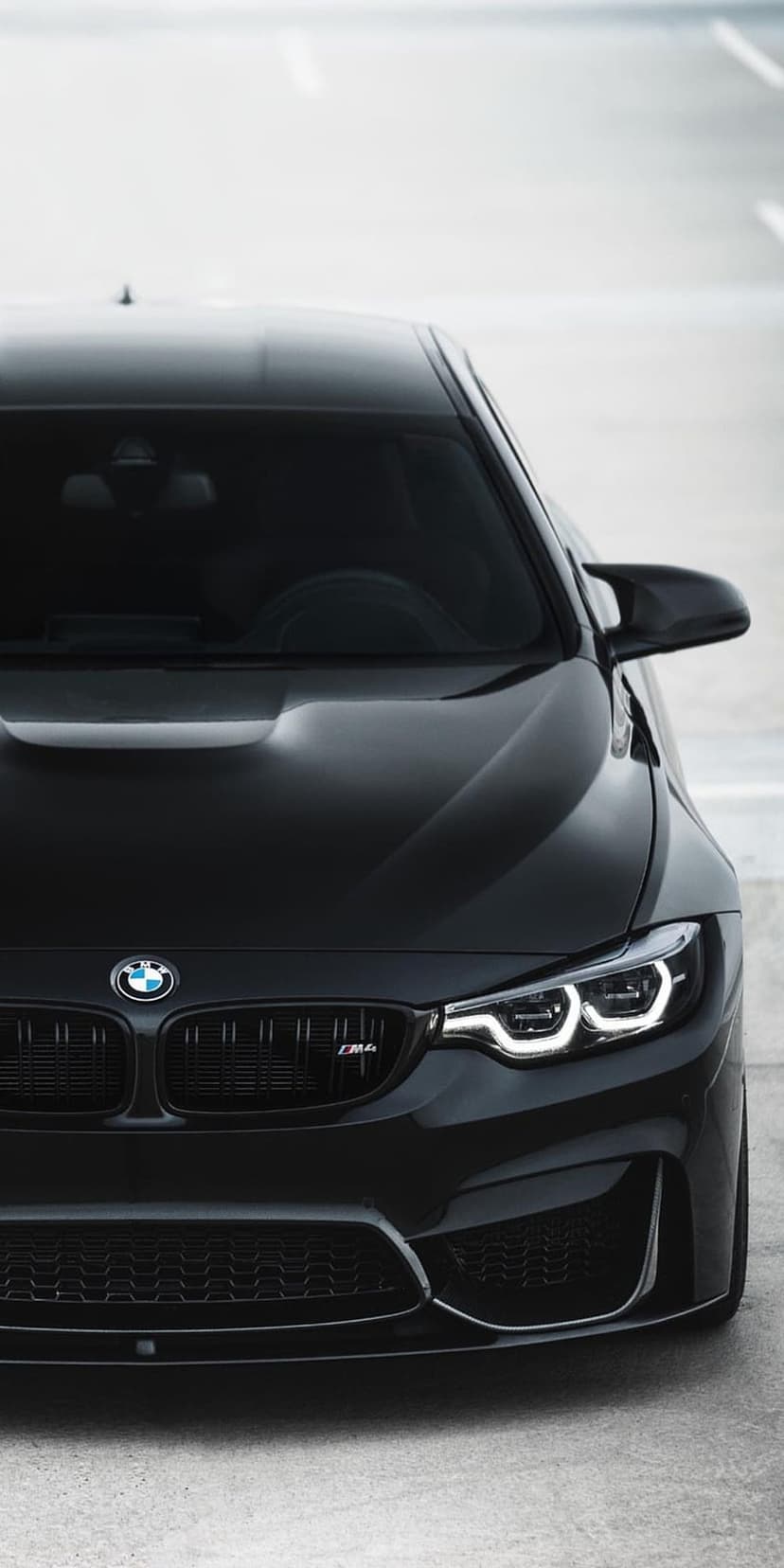 BMW M4 front grille with glowing LED headlights and a black metallic hood captured from a low perspective.