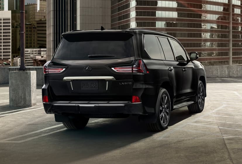 Black Lexus LX 570 SUV on a rooftop parking lot with city skyscrapers and golden hour sunlight reflections.