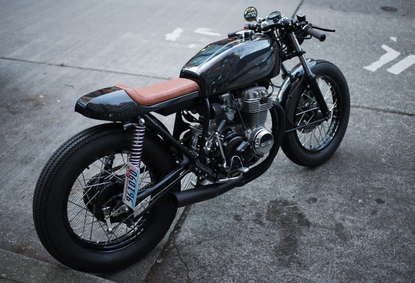 Custom cafe racer motorcycle featuring a dark glossy frame, brown leather seat, and vintage wire-spoke wheels.