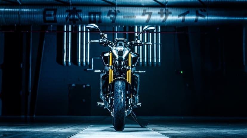 Dark Yamaha MT-09 SP motorcycle with gold forks centered in a blue industrial garage with Japanese text.