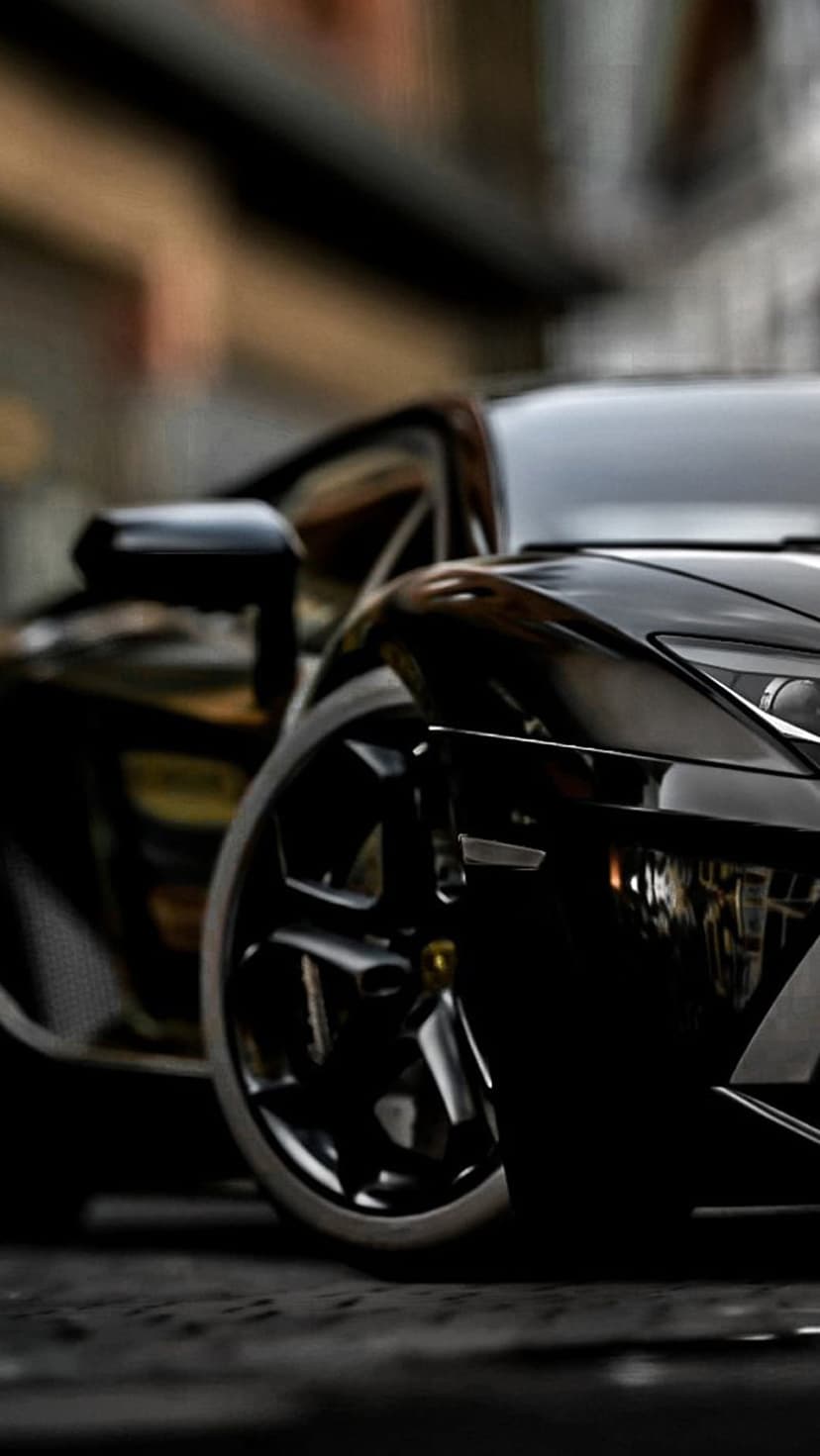 Glossy black sports car fender featuring a sharp headlight and intricate alloy wheel with reflective bodywork.