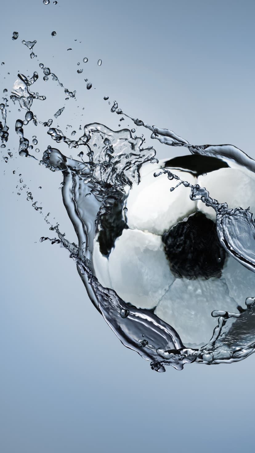Soccer ball splashing through crystalline water with exploding droplets and ripples against a dark background.