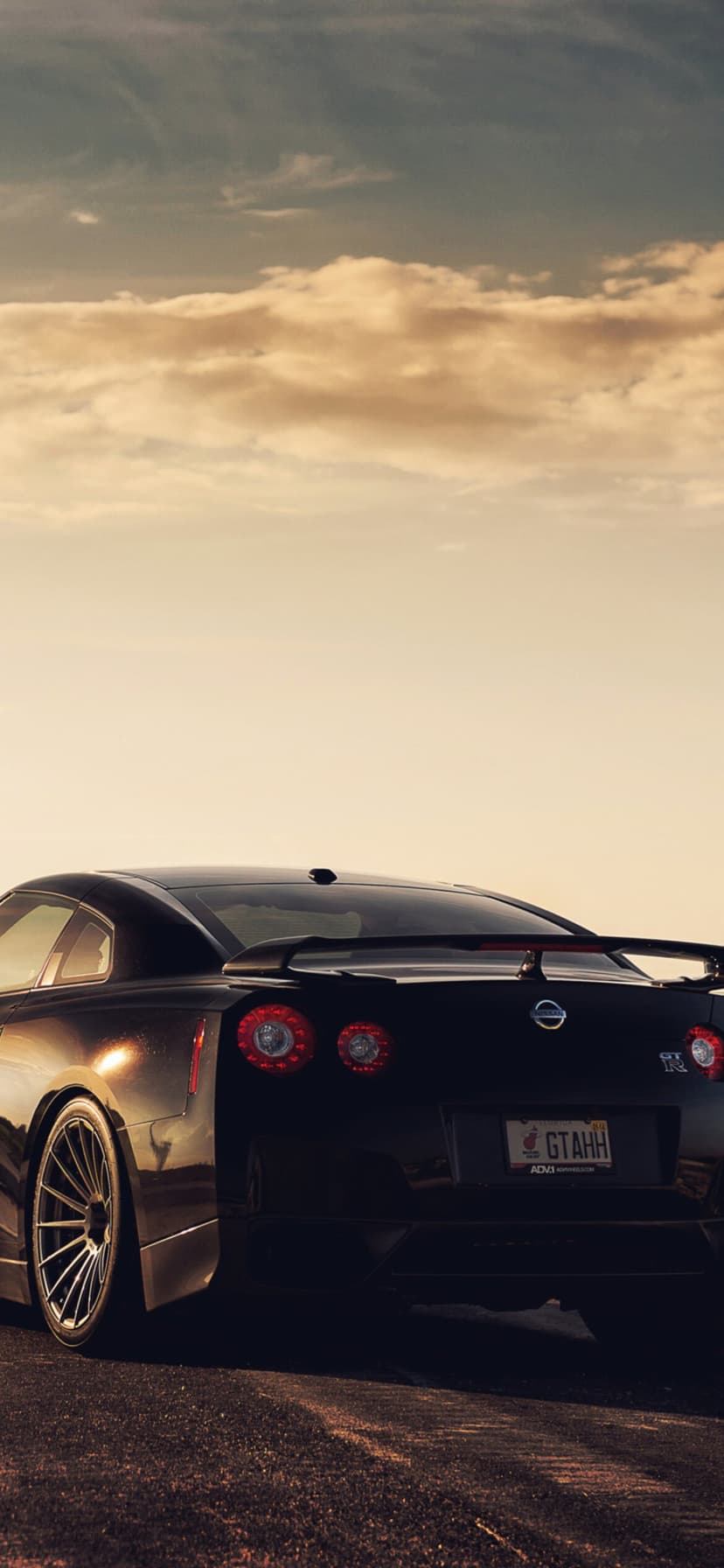 Rear view of a black Nissan GT-R with quad taillights under a golden sunset sky on a mobile screen background