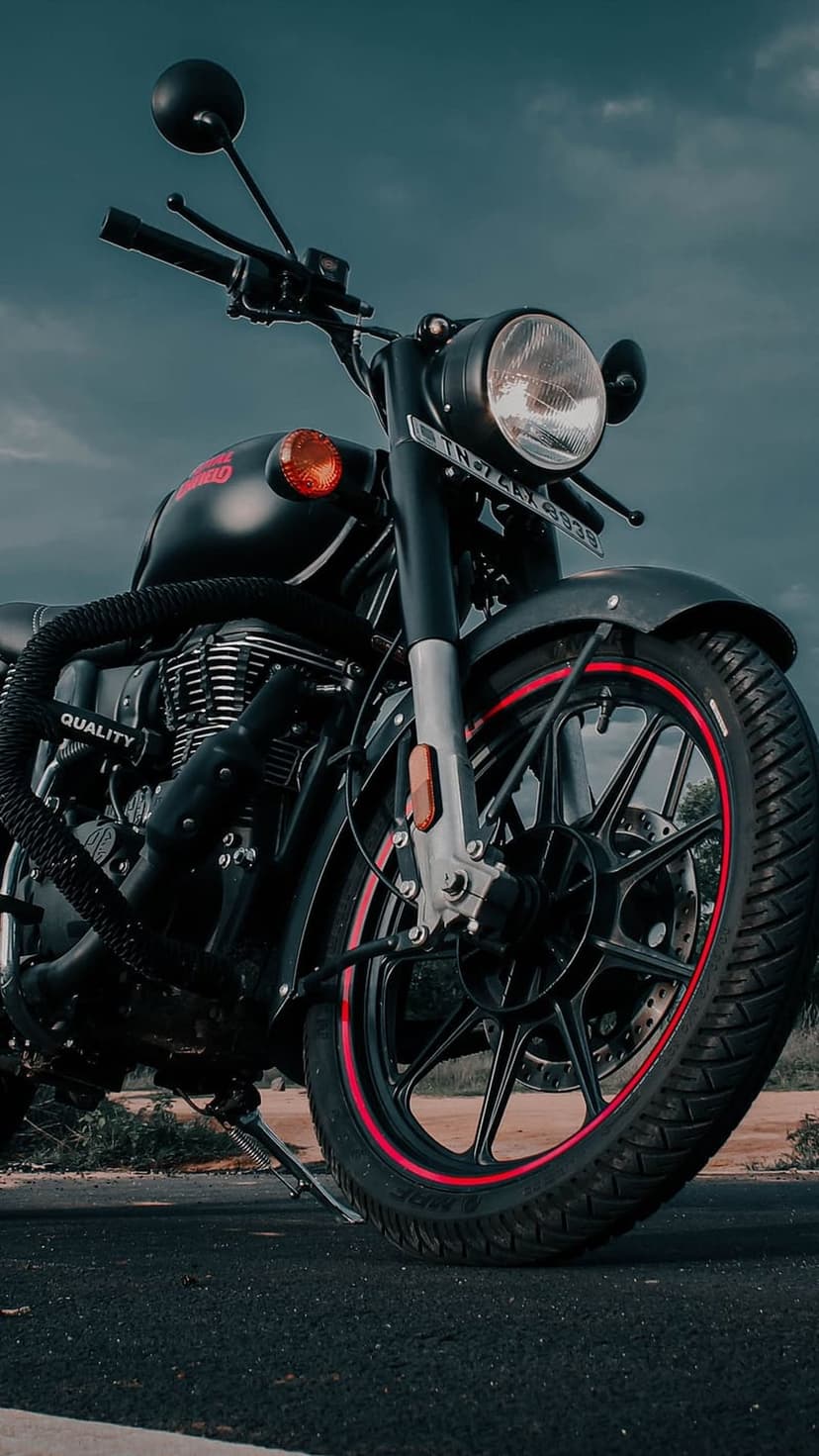 Royal Enfield front wheel and round headlight feature a red rim accent and chrome engine parts under cloudy skies.