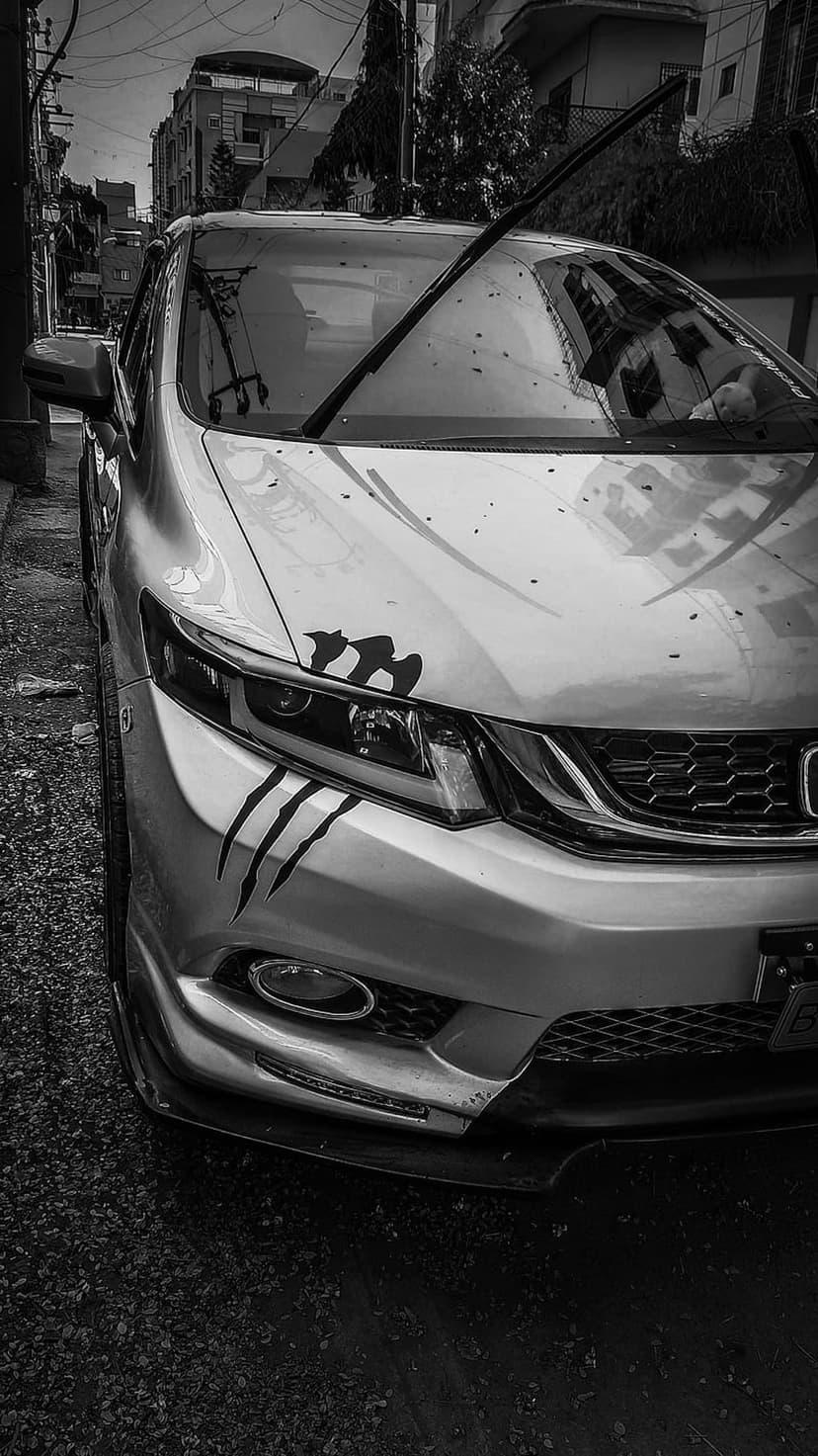 Black and white car with claw mark fender decals parked on a gravel lot under urban overhead wires at a low angle.