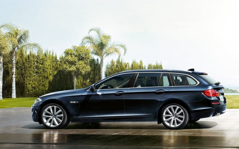 Dark blue luxury wagon parked on a reflective pavement with palm trees and a bright clear sky background.