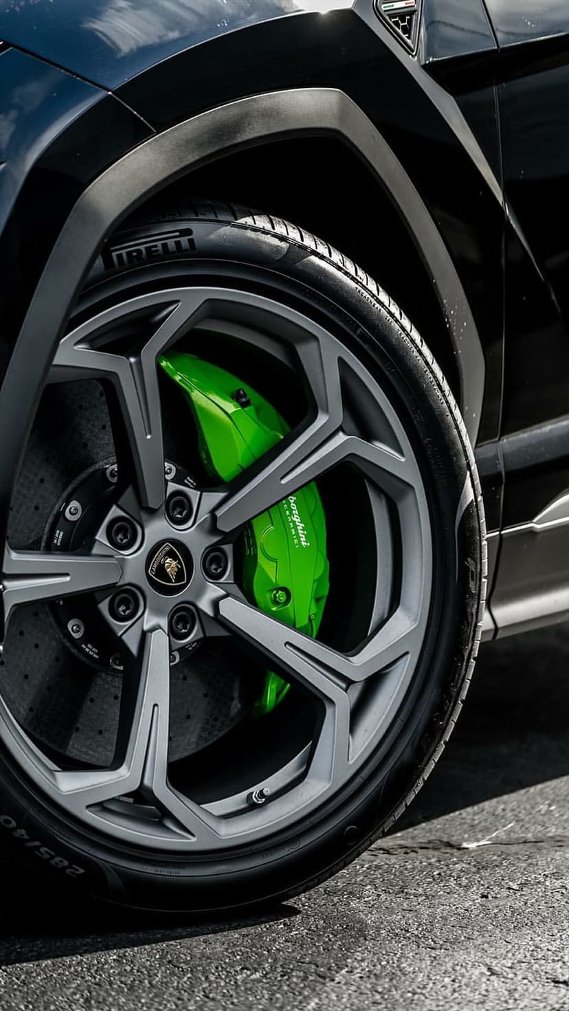 Lamborghini Urus wheel featuring green brake calipers and multi-spoke alloy rims on a textured asphalt surface.