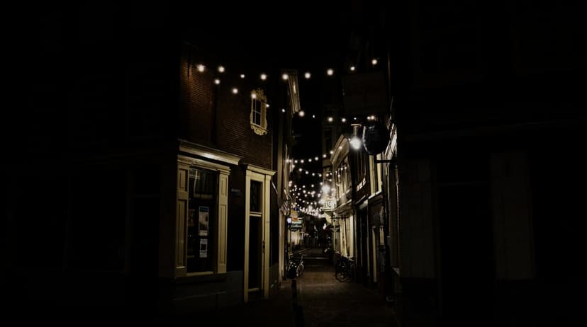 Glowing string lights hang above a narrow cobblestone alleyway between historic stone buildings at night.