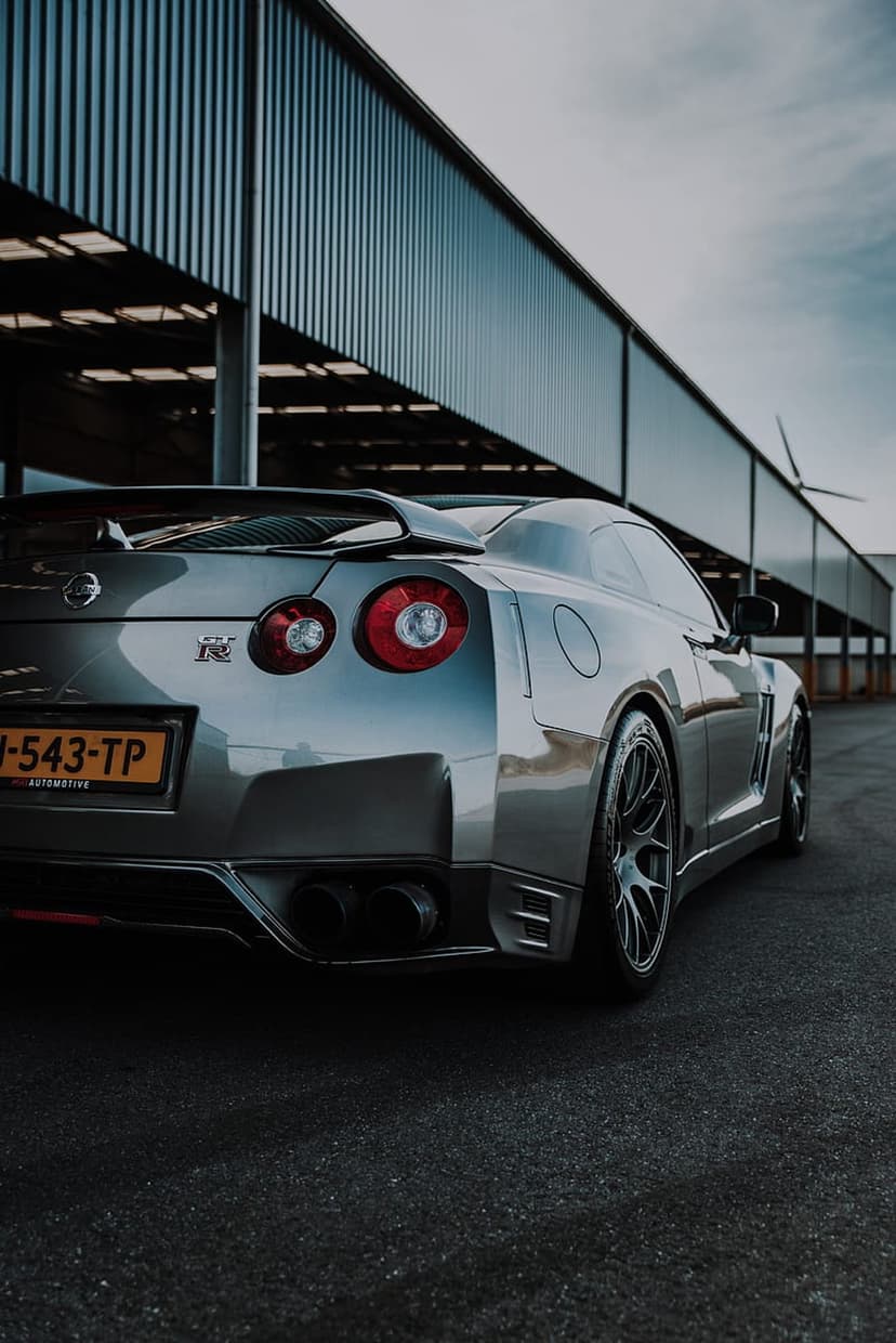 Nissan GT-R rear view with circular red taillights and quad exhausts parked against a corrugated metal wall.
