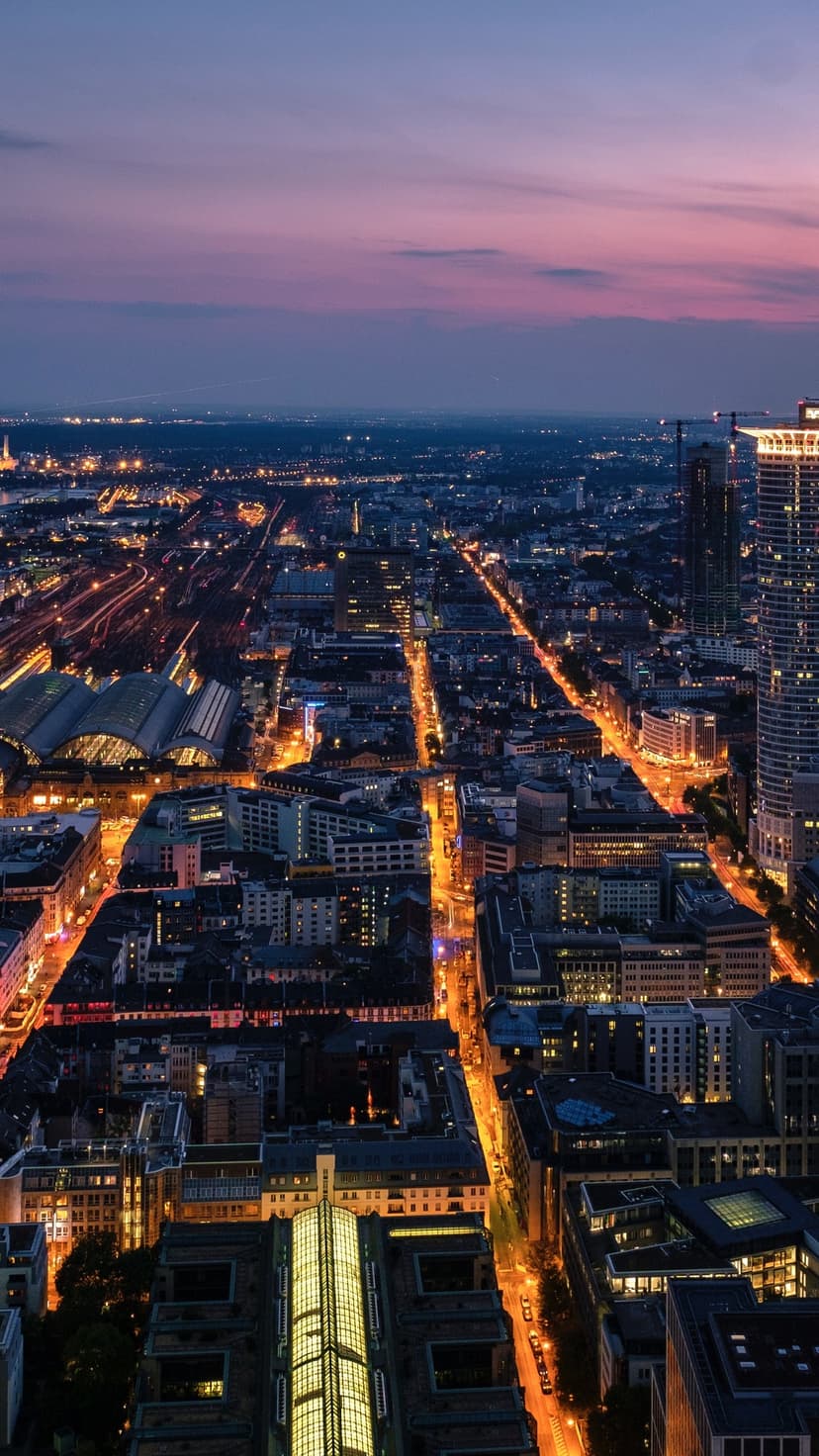 Sprawling city streets glow with golden lights under a deep purple twilight sky from a high aerial view.