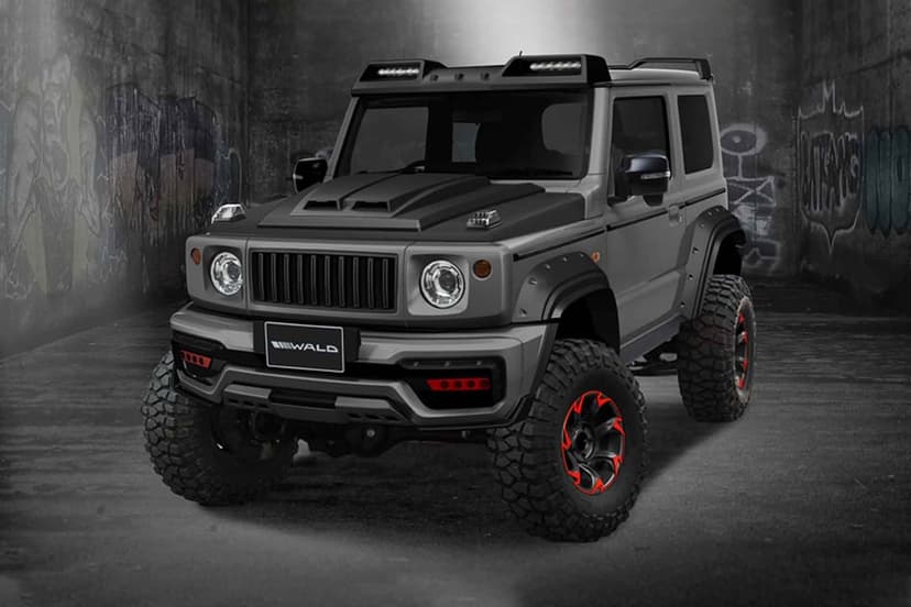 Grey Wald Suzuki Jimny with knobby tires and red accents parked in a dark urban alley with graffiti walls.