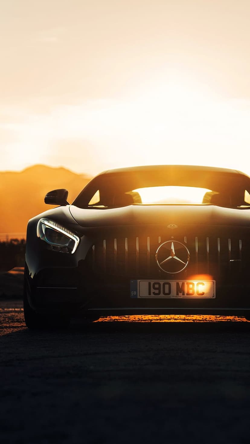 Black Mercedes-AMG GT front grille and headlights reflecting golden sunset light against mountain peaks.