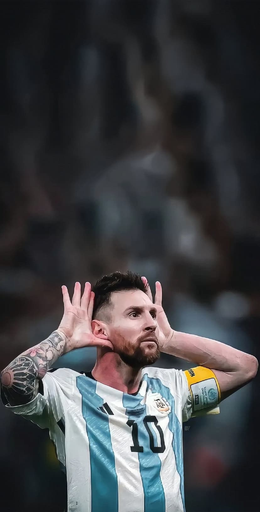 Lionel Messi in a blue and white Argentina jersey celebrates a goal with hands raised on a blurred pitch.