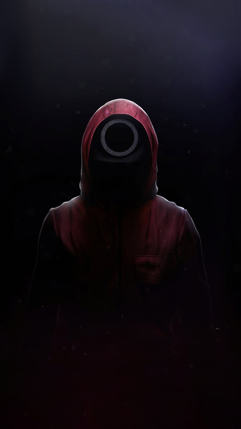 Masked person in a crimson red hoodie with a black circle mask standing in deep, high-contrast shadows.