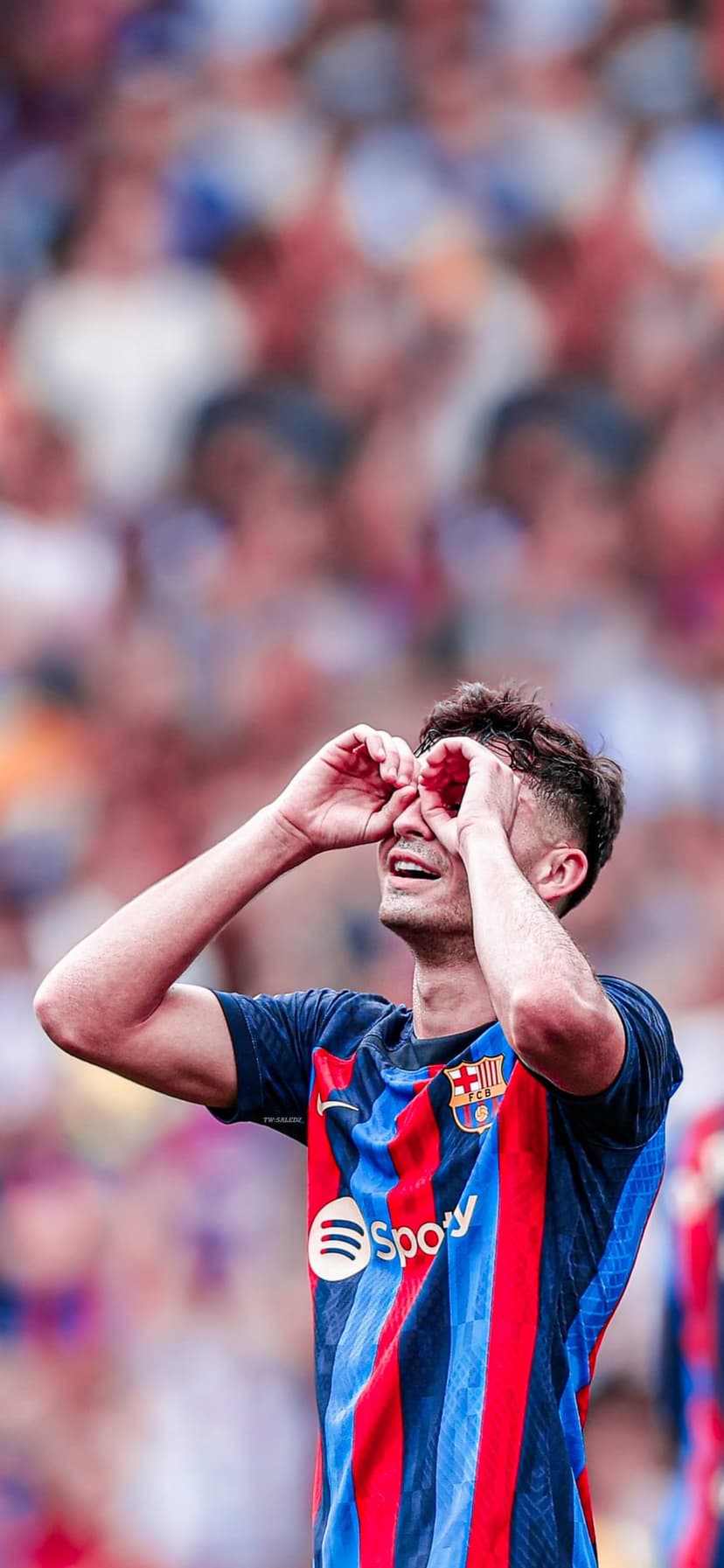 Pedri performs a binoculars hand gesture celebration while wearing a blue and red striped Barcelona jersey.