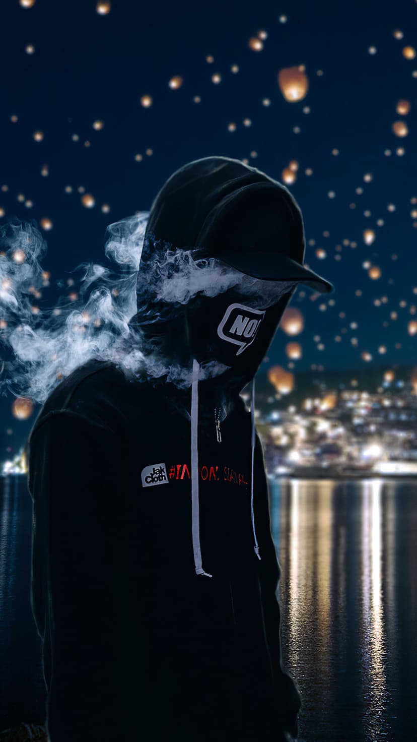 Shadowy figure in a hoodie and cap stands before a lake as glowing lanterns float over a distant city at night.