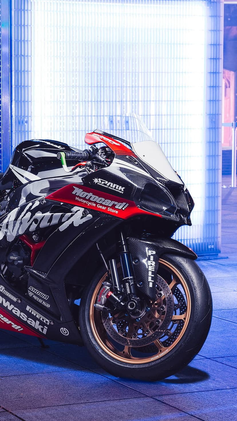 Kawasaki Ninja sportbike with red and black fairings parked in front of a glowing neon blue background.