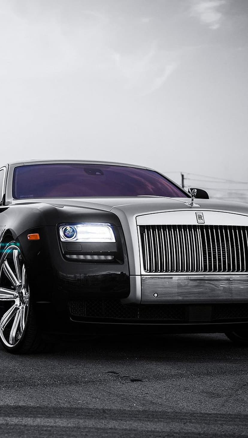 Rolls-Royce Ghost luxury car with a chrome grille and Spirit of Ecstasy hood ornament on dark asphalt.