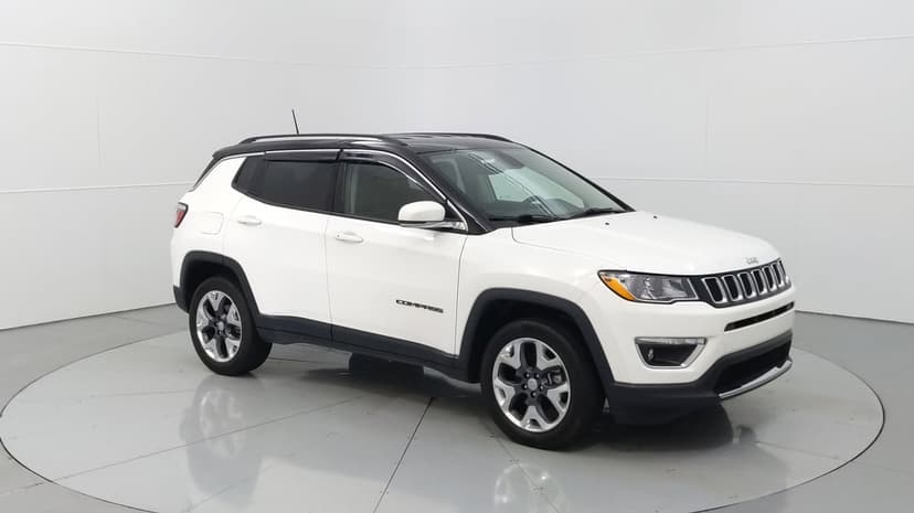 White Jeep Compass SUV parked in a bright studio with reflective floors, black roof accents, and alloy wheels.