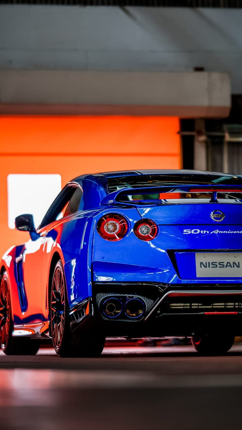 Blue Nissan GT-R 50th Anniversary Edition rear view featuring quad taillights and a spoiler on an orange backdrop.