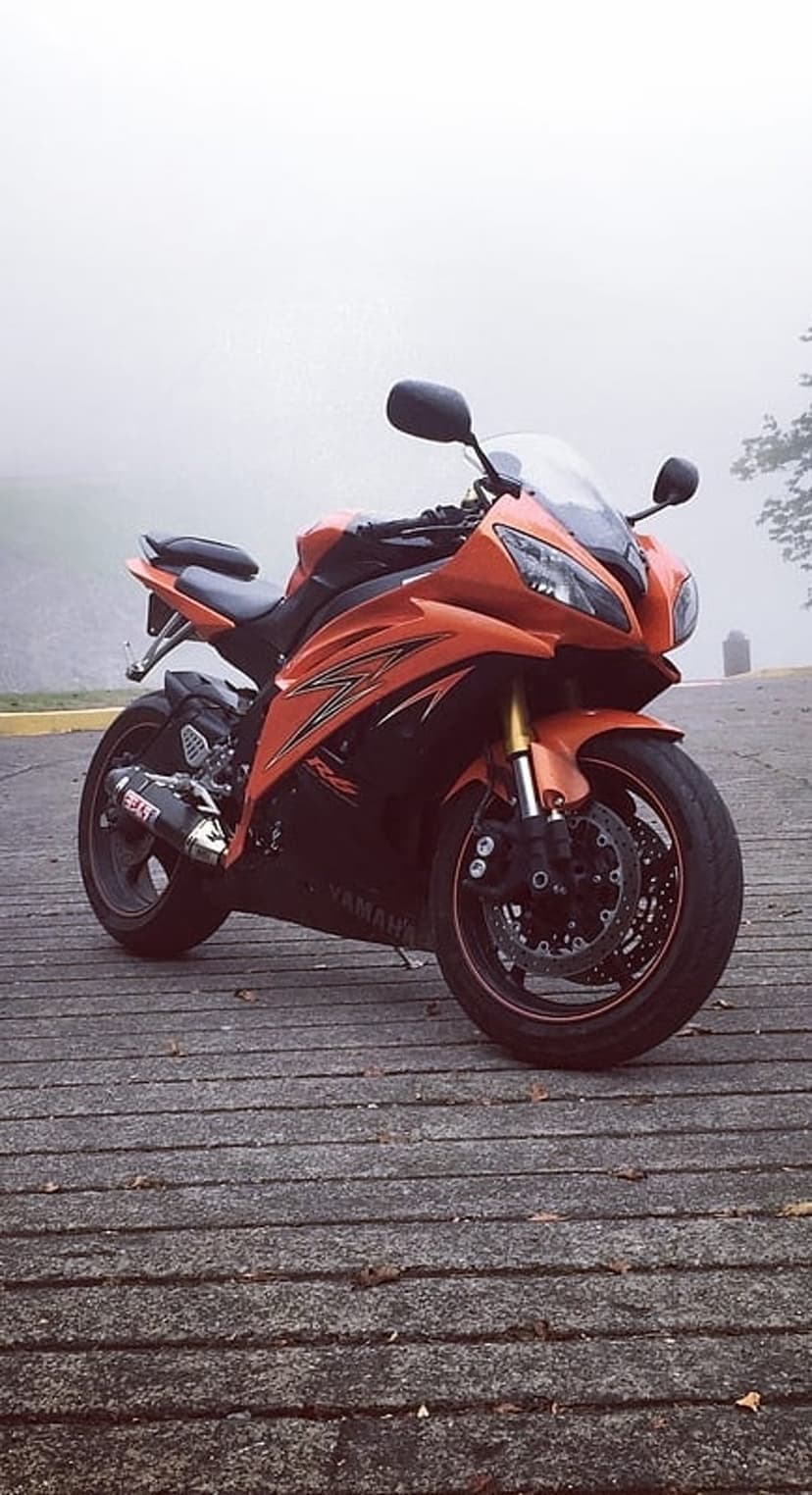 Orange Yamaha R6 motorcycle parked on a wooden dock surrounded by heavy white mist in a portrait orientation.
