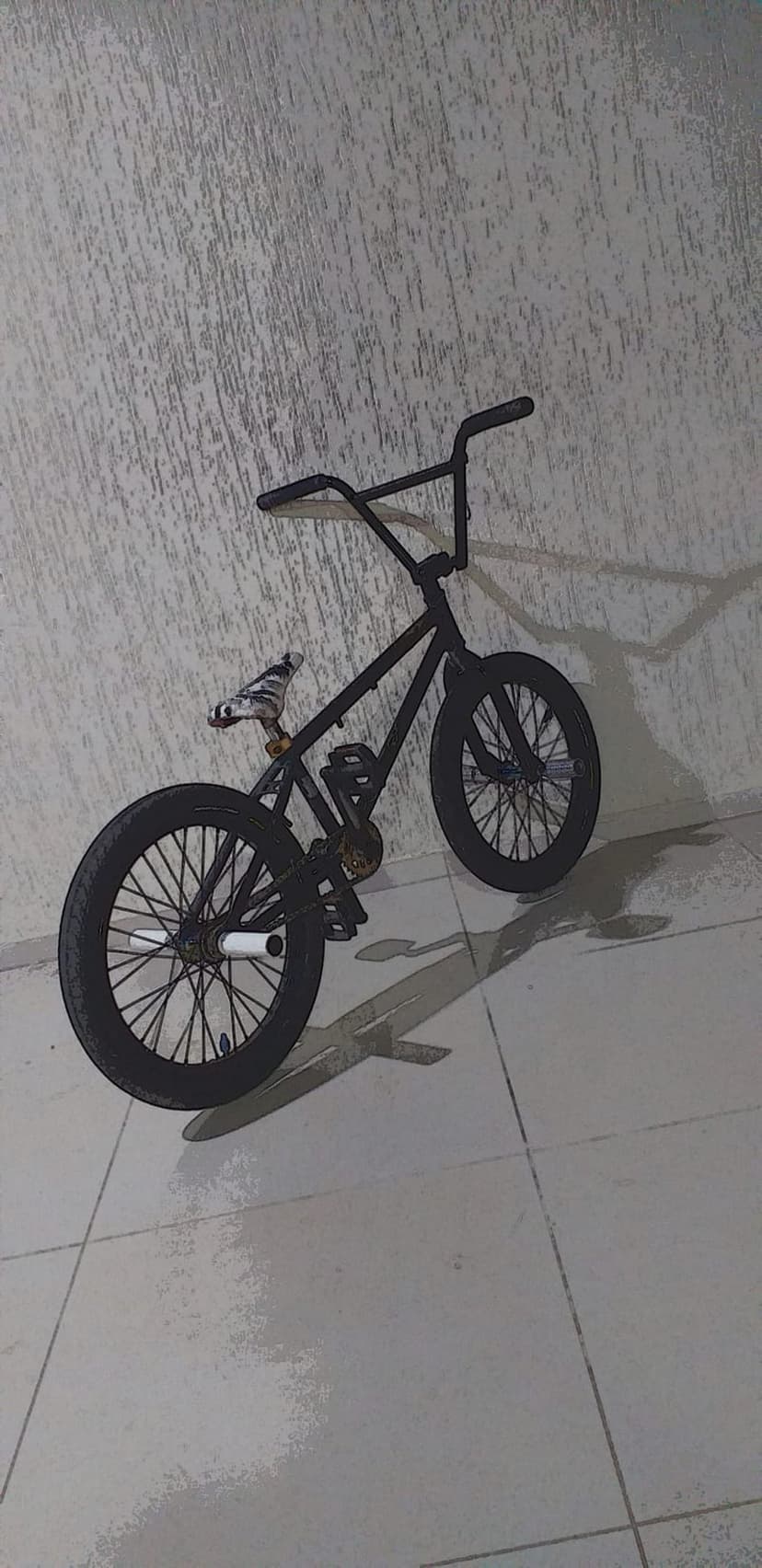 Black BMX bicycle rests against a textured stone wall with sharp shadows stretching across the tiled ground.