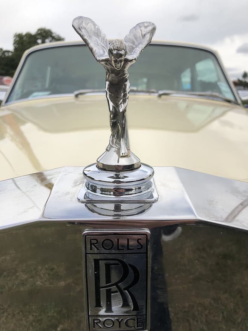 Spirit of Ecstasy figurine with wings outstretched above a silver Rolls-Royce badge on a cream vintage car hood.