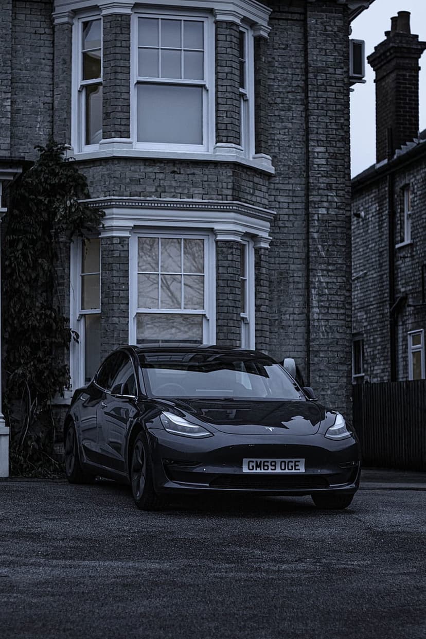 Polished black Tesla electric car parked against the background of a historic red brick Victorian residence.