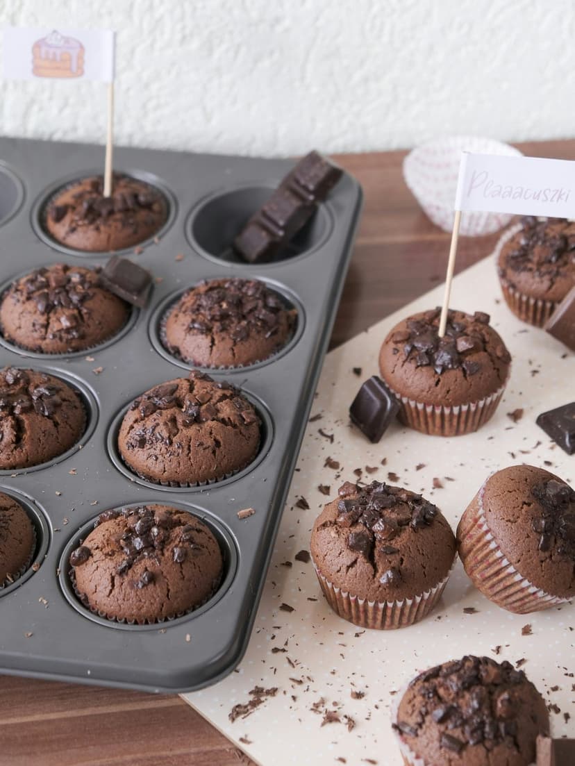Chocolate chip muffins in a metal tin decorated with tiny flags and surrounded by dark chocolate chunks.