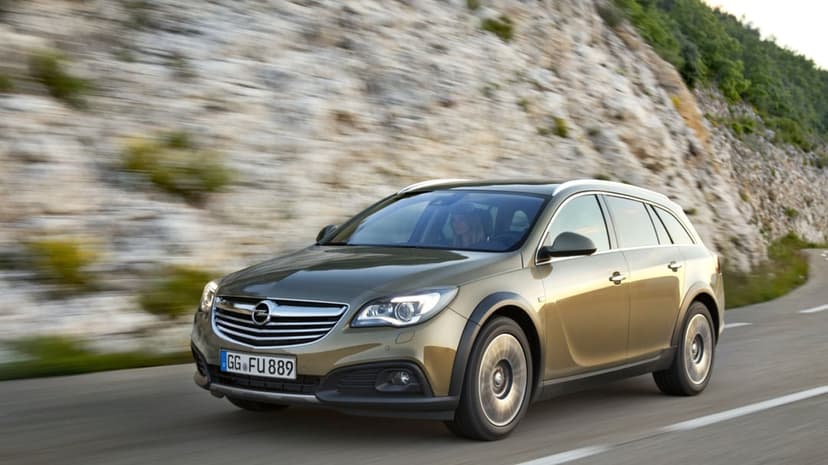 Gold Opel Insignia Country Tourer driving on a winding road with motion blur against a rocky cliff background.