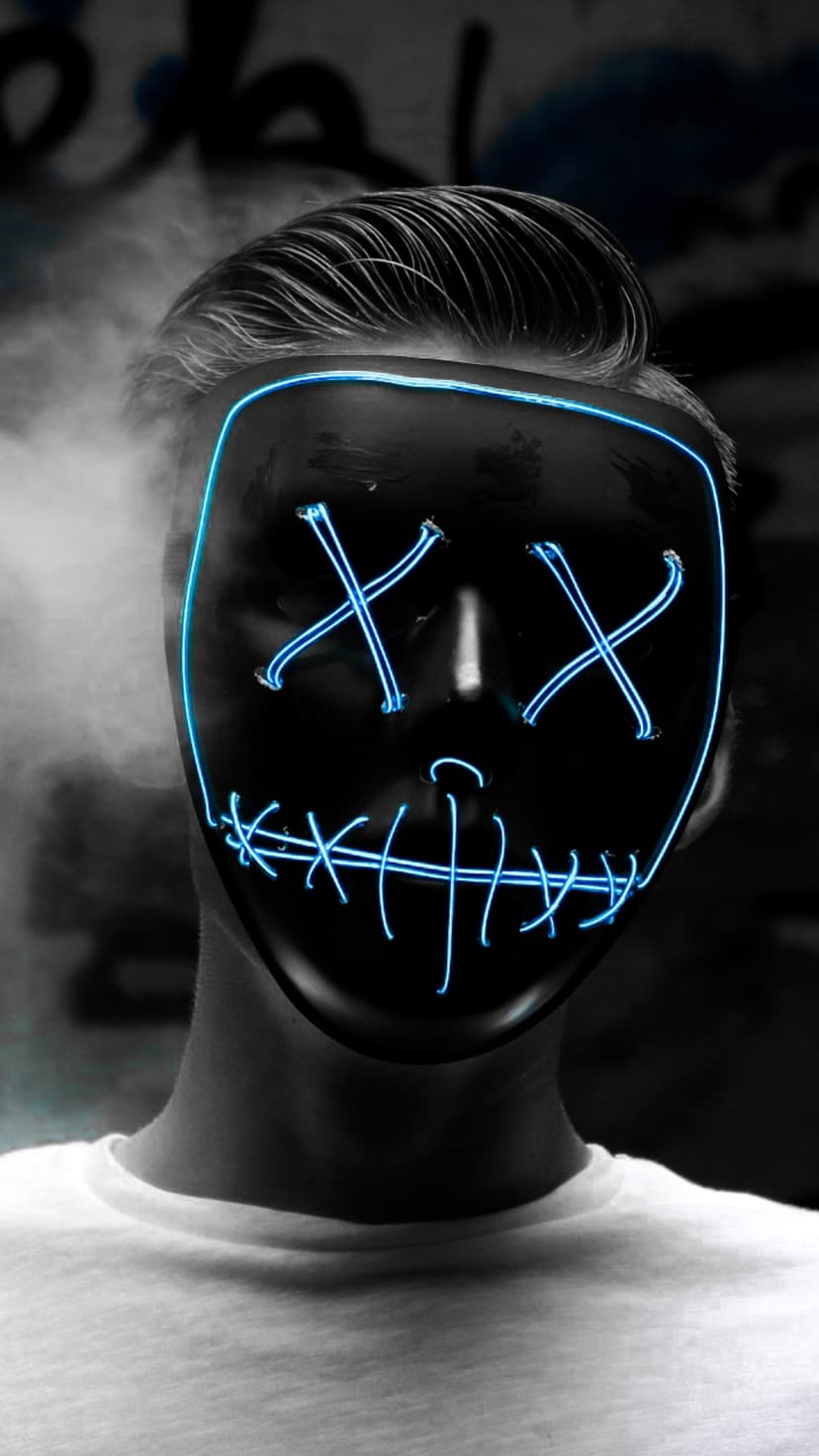 Person wearing a black mask with blue neon X eyes and a stitched smile surrounded by grey smoke and city textures.