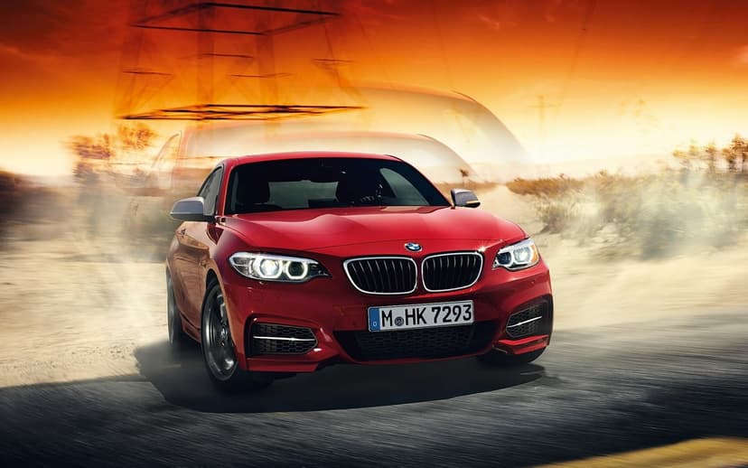Red BMW sports car speeding on a dusty road with motion blur under an orange sunset sky and power lines.
