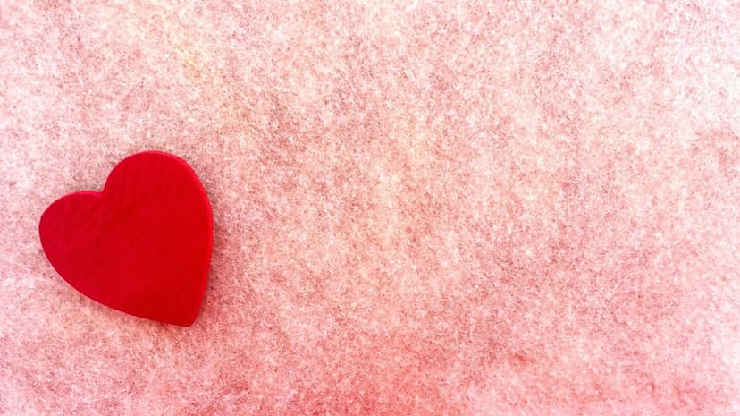 Red heart resting on a fuzzy pink fabric surface with soft shadows and a plush, tactile texture.
