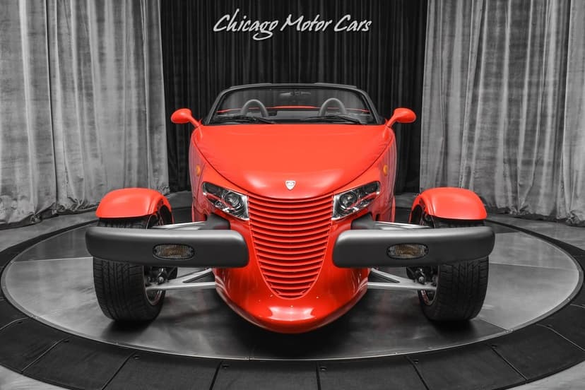 Front view of a red Plymouth Prowler with open wheels and black bumpers in a luxury car showroom studio.