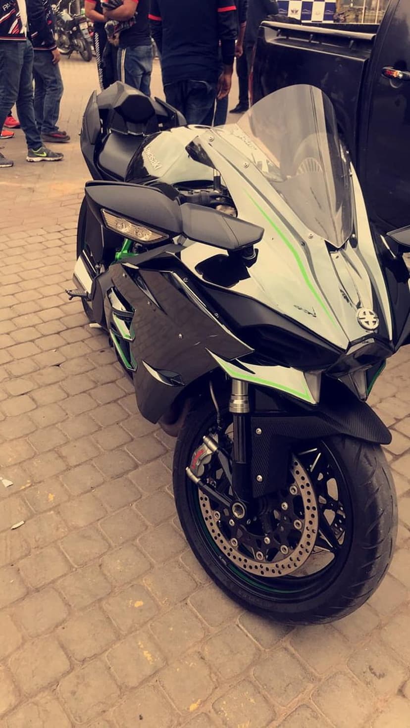 Kawasaki Ninja H2R motorcycle with green accents and carbon fiber bodywork parked on a grey paved road surface.