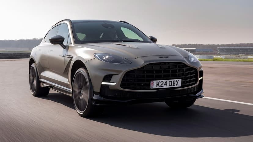 Satin titanium Aston Martin DBX707 driving fast on a race track with visible motion blur.
