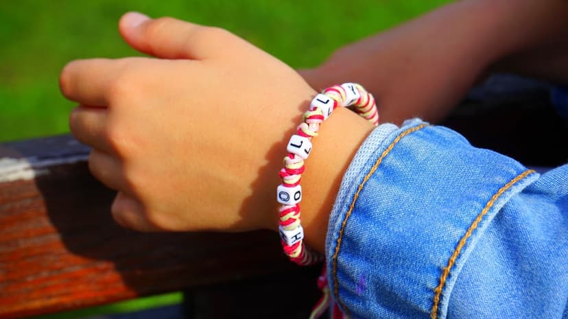 Alphabet bead bracelet on a child's wrist with a denim jacket and soft green outdoor bokeh background.