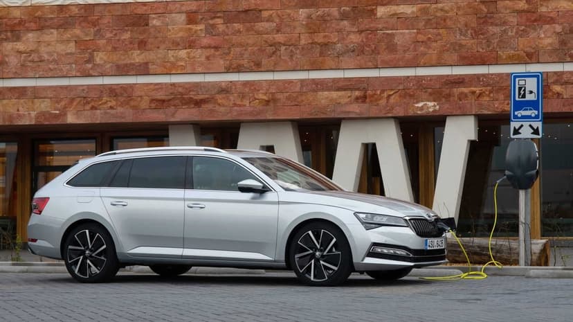 Silver station wagon charging at an EV station with a yellow cable against a brown stone wall.