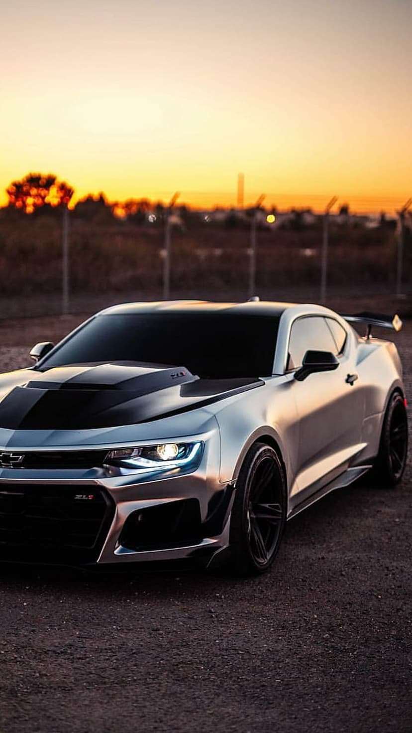 Silver Chevrolet Camaro ZL1 drifting on a track during a golden sunset with tire smoke and warm evening light.