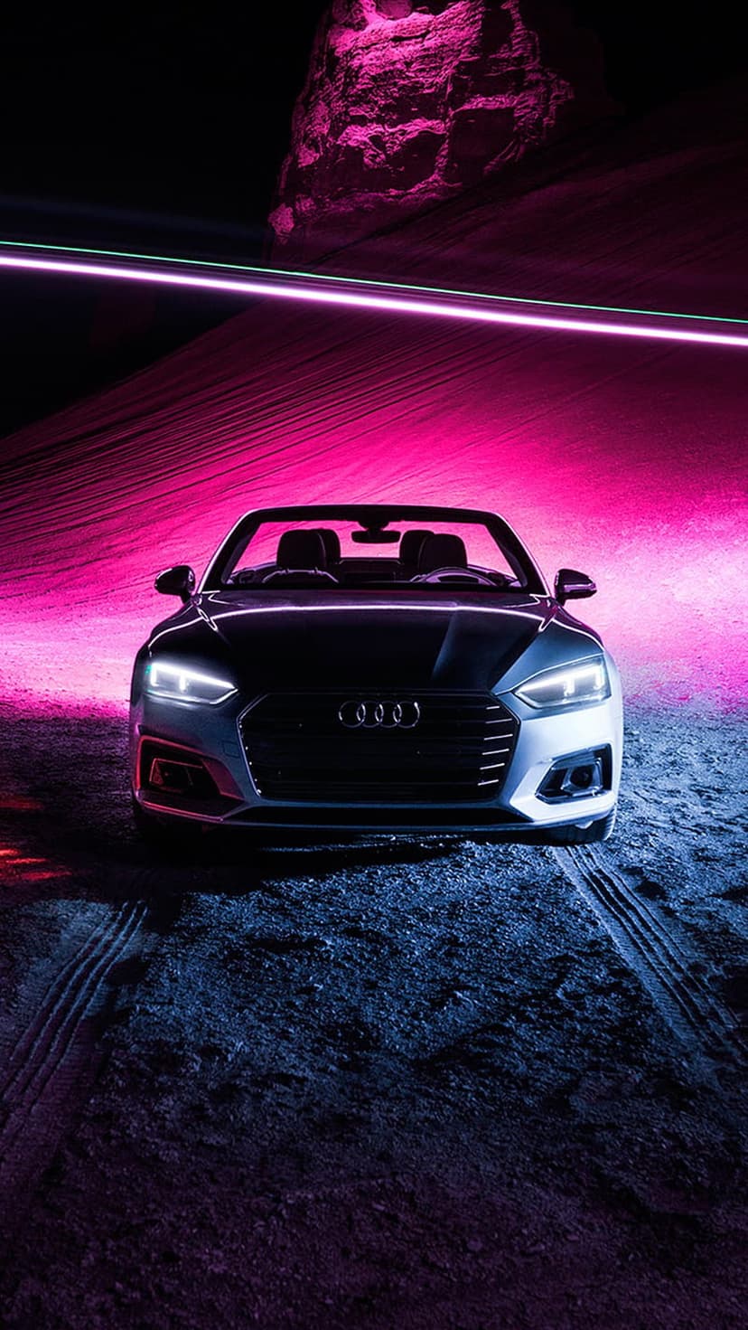 Audi convertible sports car with glowing headlights on wet desert ground under pink and blue neon lighting.
