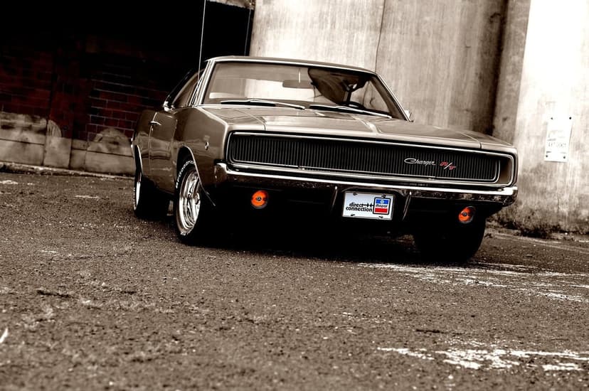 Classic 1968 Dodge Charger R/T with glowing amber lights parked on asphalt against a weathered concrete wall.