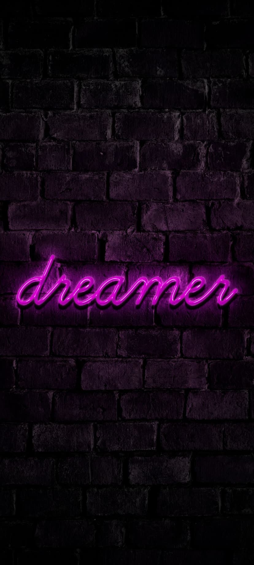 Purple neon sign spelling Dreamer mounted on a dark textured brick wall with a soft violet ambient glow.