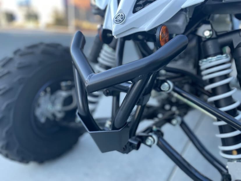 White Yamaha ATV front bumper and suspension with matte black bull bar and coilover shocks in daylight.