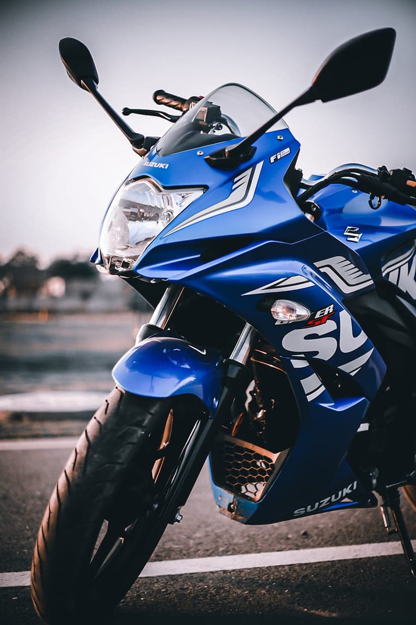 Blue Suzuki sportbike front fairing and headlights on asphalt with road markings under an overcast sky.