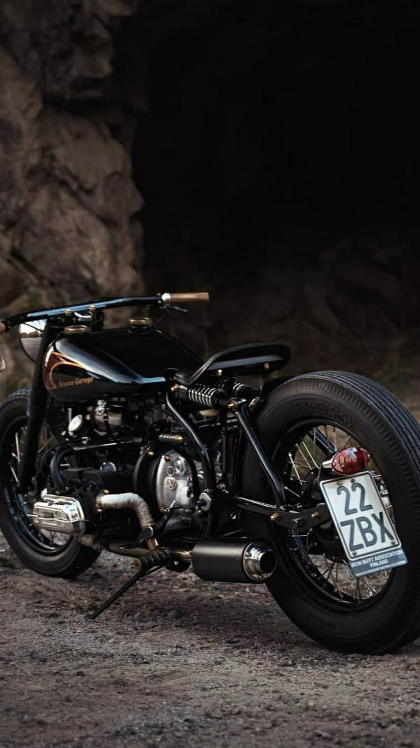 Custom black bobber motorcycle with copper accents and fishtail exhaust parked on a dark, rocky mountain path.